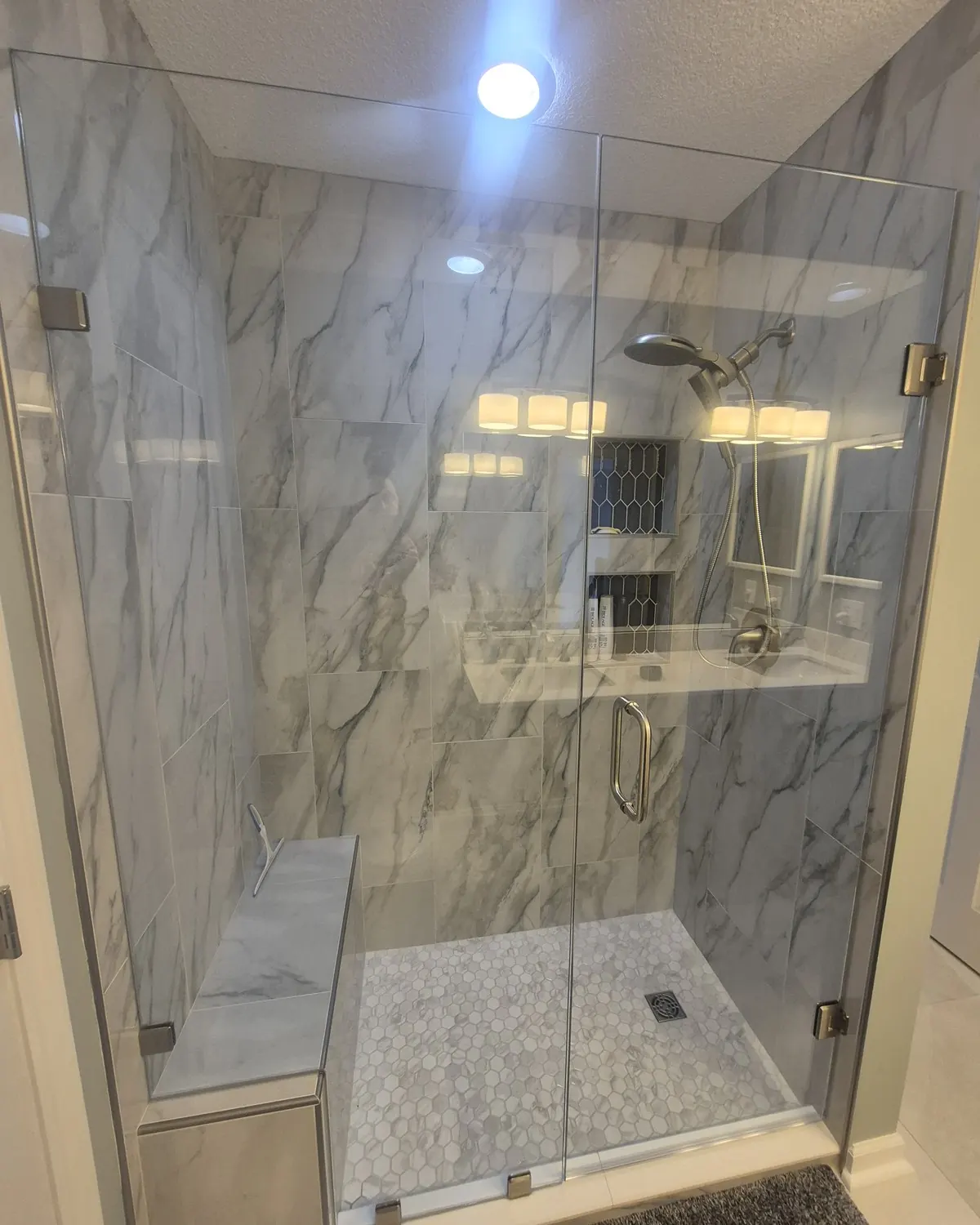 Completed walk-in shower with built-in bench, marble tile, and frameless glass door